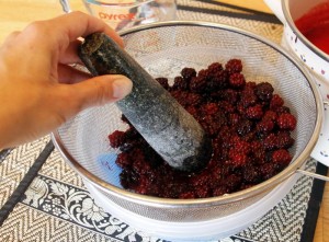 crushing blackberries through a sieve with a pestle