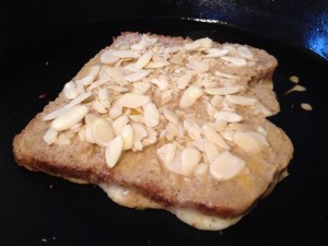 french toast cooking in pan with almonds on top